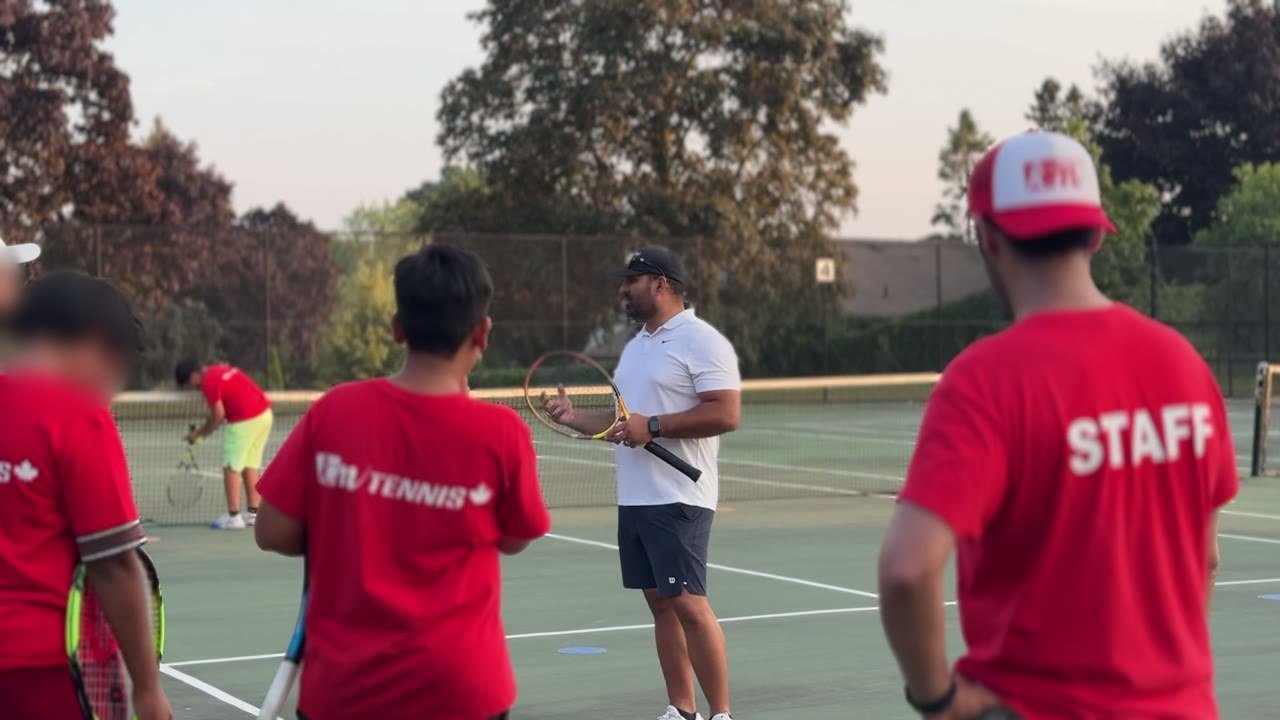 Young children rallying on small courts with low nets in a white indoor tennis dome, with coaches in ICM red.