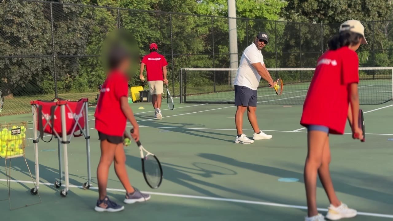 Children rallying over a low net on the middle courts of a white indoor tennis dome.