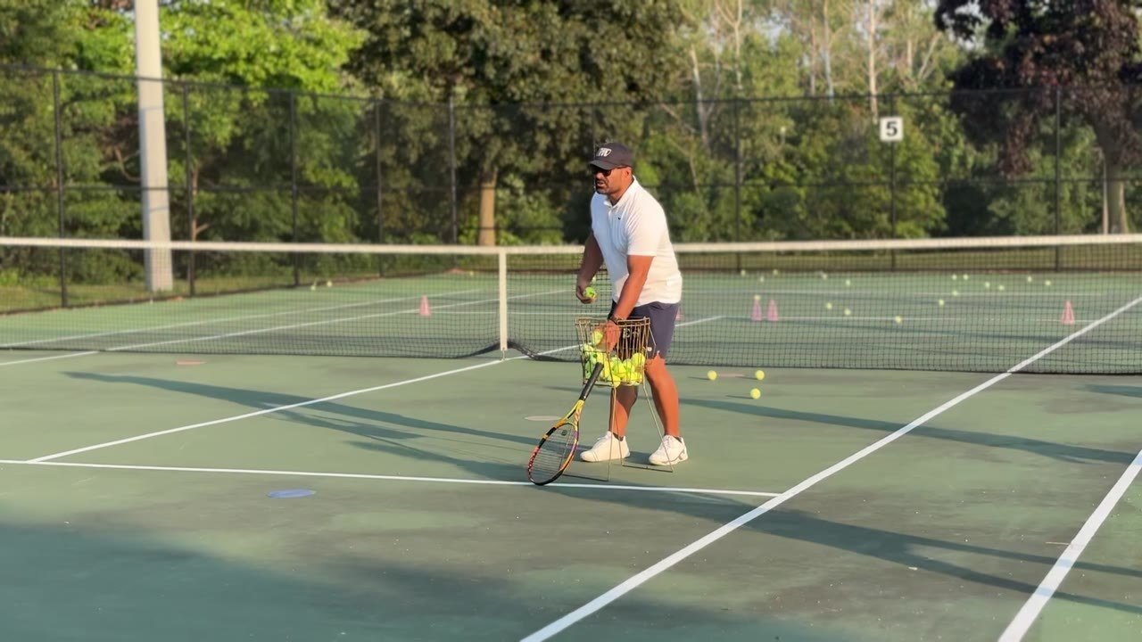 Full-size green courts in an indoor tennis dome, with a junior player and coaches in red.