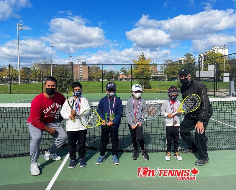 Two coaches and four young medal winners at the net of an outdoor court.