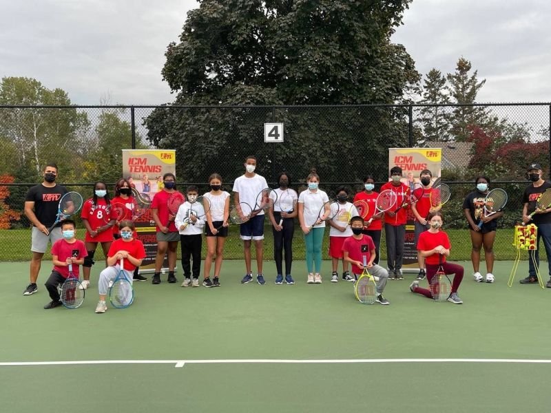 A group of young players and coaches on an outdoor court in Oshawa, some kneeling with medals.