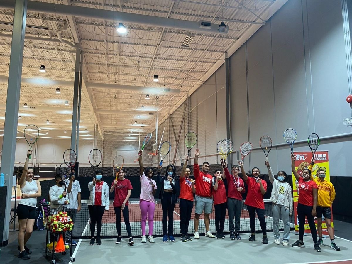 Players and the coach in a line raising their racquets, some with medals, beside an ICM banner in the indoor facility.
