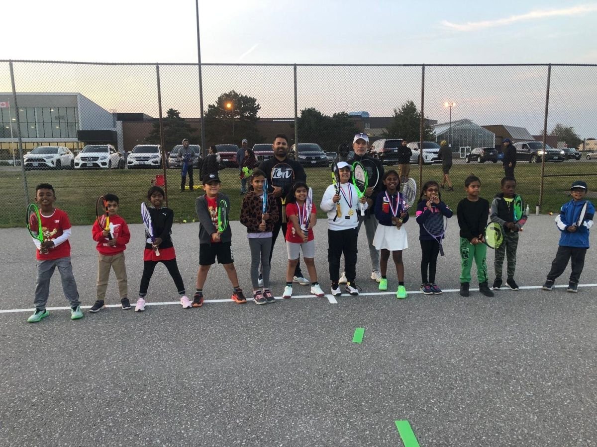 Young players with medals lined up with two coaches on an outdoor court at dusk.