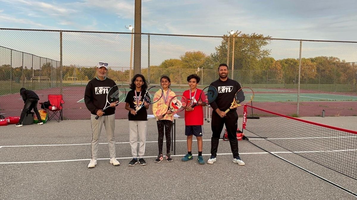 ICM coaches and young players with medals on an outdoor court at sunset.