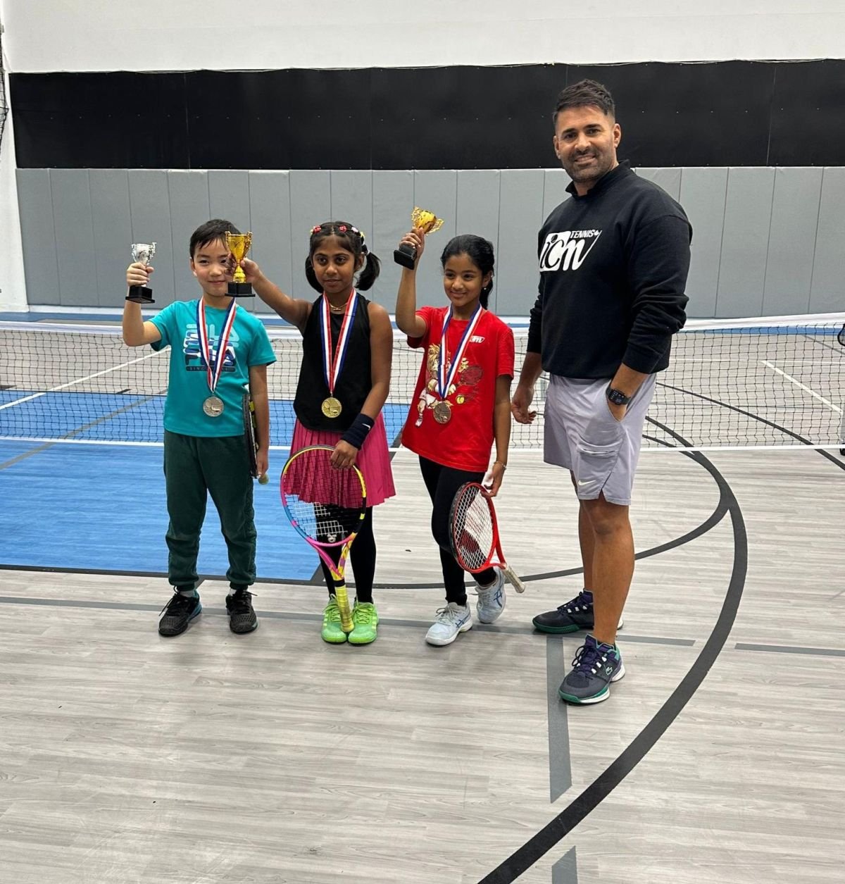 An ICM coach with three young trophy winners on an indoor court.