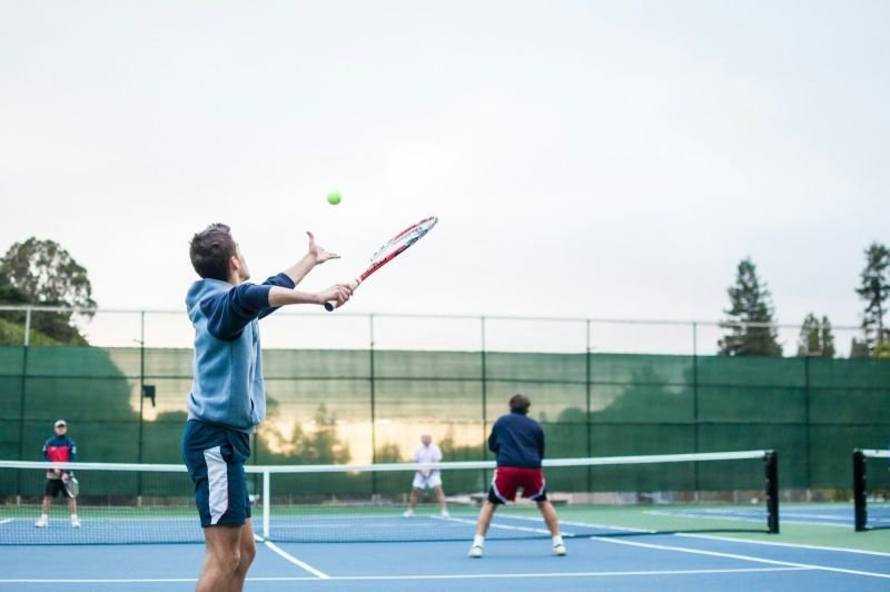 An adult player serving in a doubles game on an outdoor court.