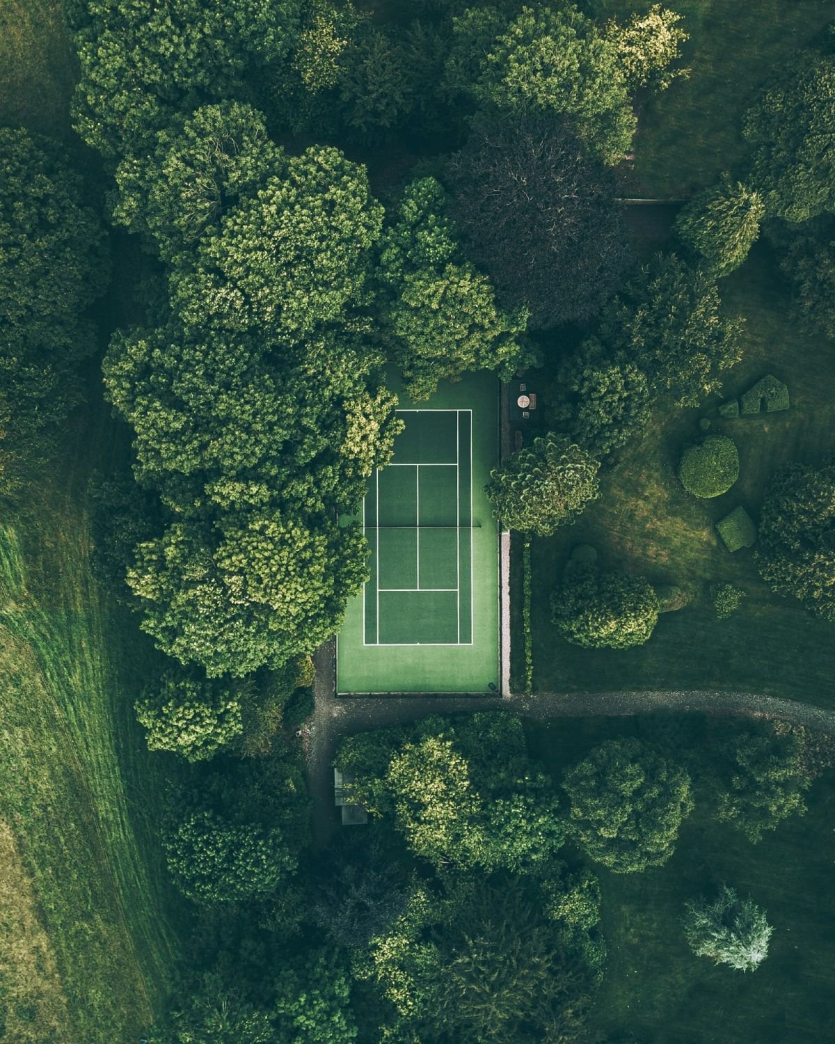 An aerial view of an outdoor tennis court surrounded by trees.