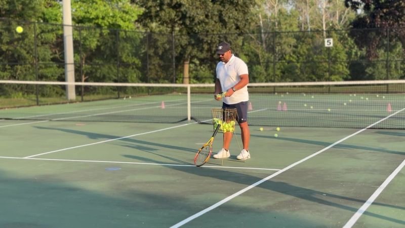 An ICM coach feeds balls from the net on an outdoor court.