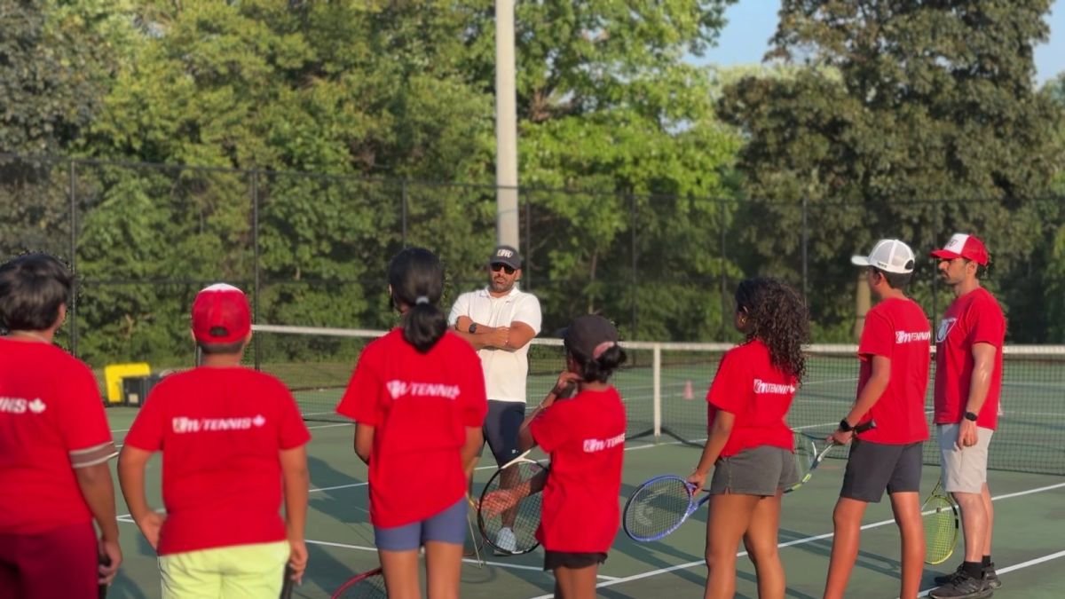 A group of ICM juniors with their racquets listens to the coach at the net.