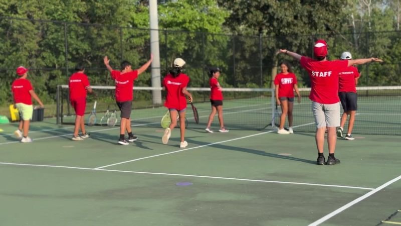 ICM juniors and a coach cheer together at the end of a session on an outdoor court.